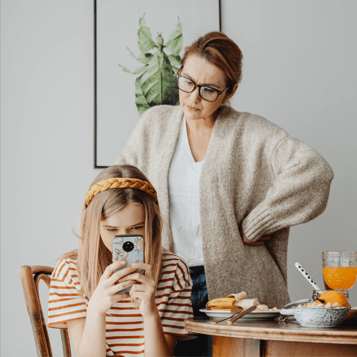 Madre observando a su hija mientras utiliza un teléfono móvil